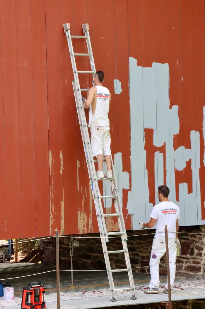 services-04 Two men repainting a large wall using a ladder, engaged in renovation work outdoors.
