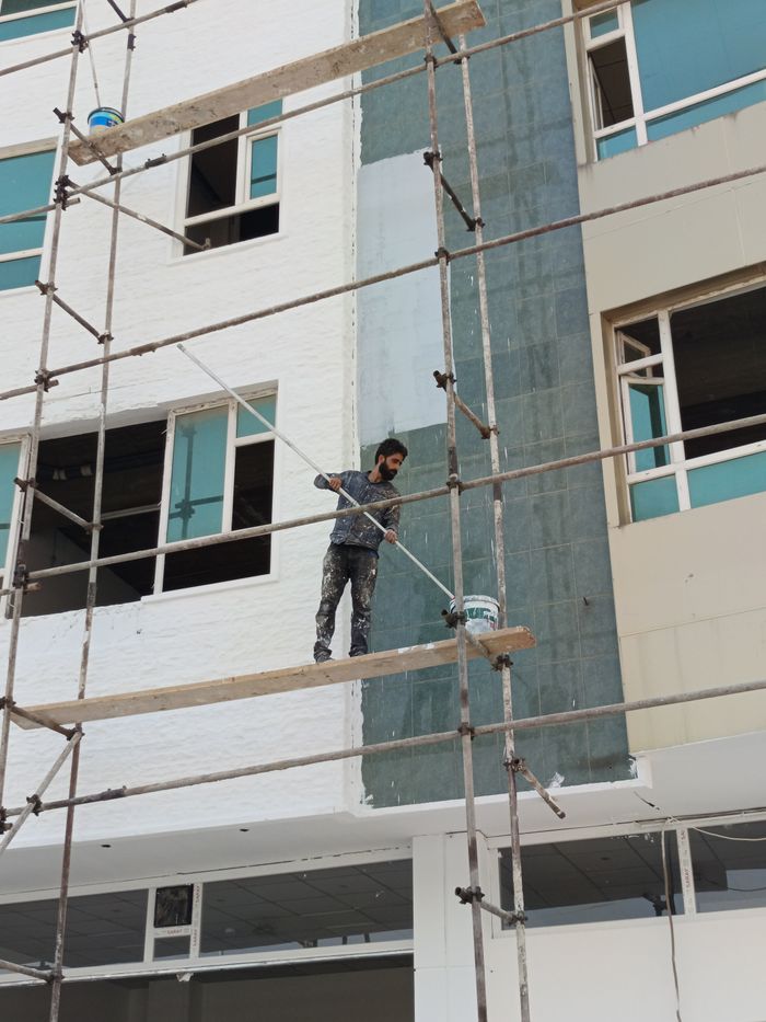 services-01 Construction worker on scaffolding painting a building exterior.