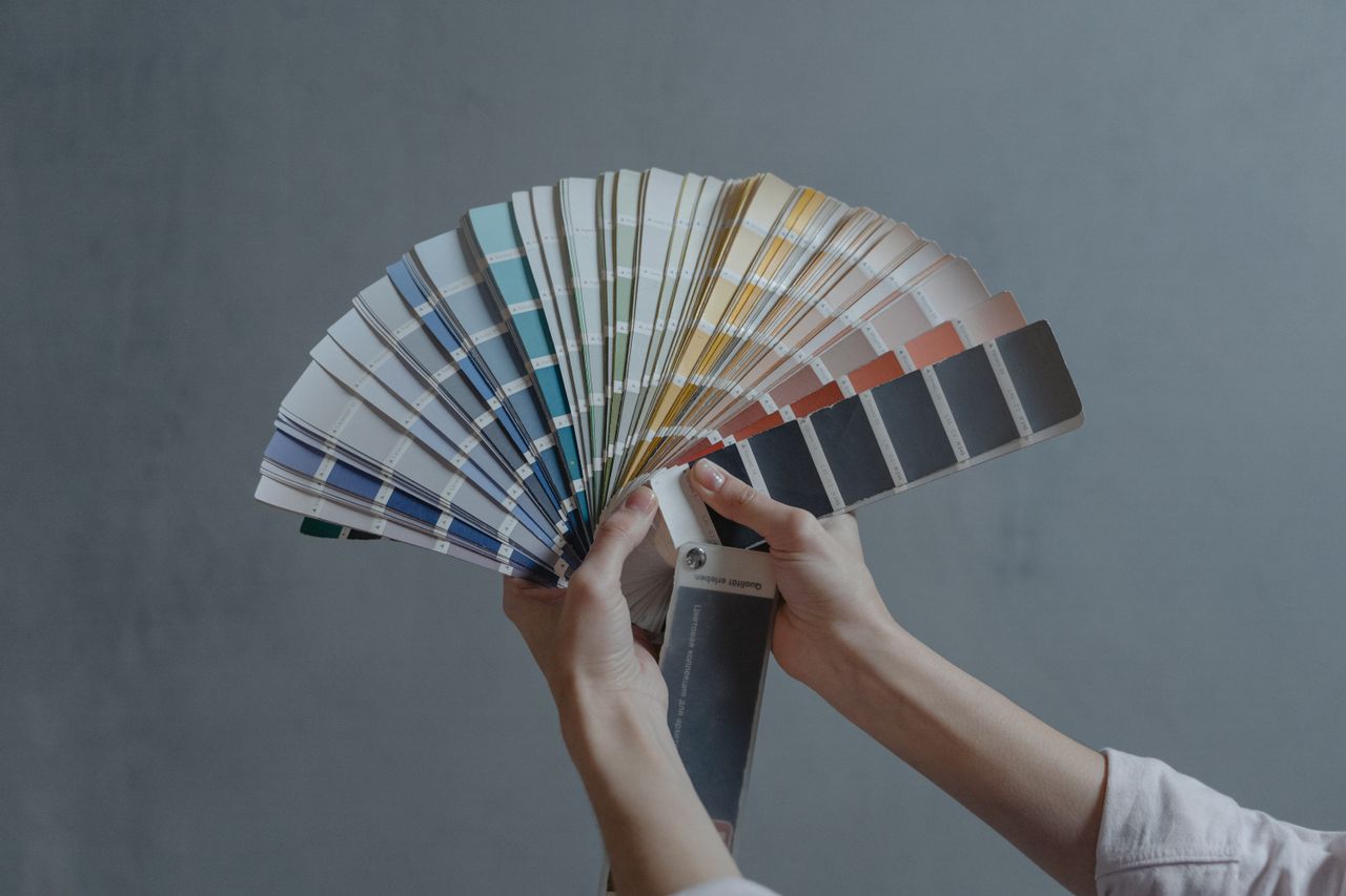 gallery-4 Hands holding a colorful fan of swatches on a gray backdrop, ideal for design themes.